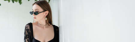 Pretty woman in sunglasses and guipure robe standing near wall at resort, bannerの写真素材