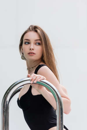Pretty and stylish woman in black swimsuit touching handrails at resort