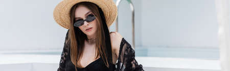 Fashionable woman in swimsuit and straw hat looking at camera at resort, banner