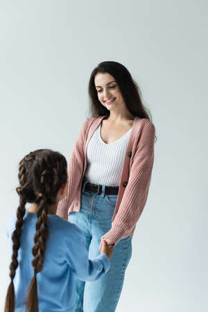 happy brunette woman holding hands of daughter isolated on grey