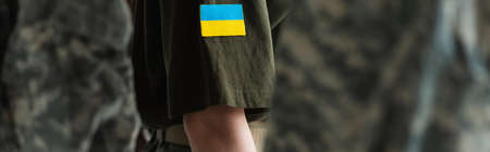 Cropped view of servicewoman with ukrainian flag on chevron standing near soldiers, banner