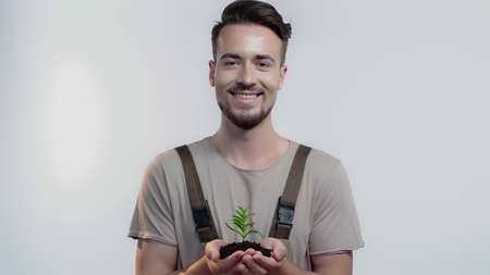 Smiling gardener holding soil and plant on grey backgroundの写真素材