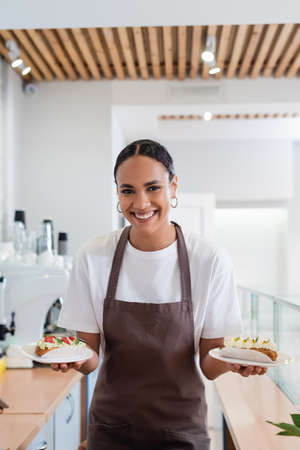 Positive african american seller holding dessert and looking at camera in sweet shop