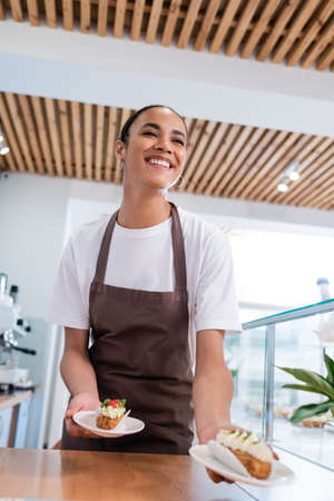 Low angle view of african american seller holding eclairs in confectioneryの写真素材