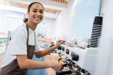 Cheerful african american barista making coffee and looking at camera in confectioneryの写真素材