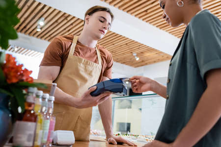 Low angle view of african american customer paying with credit card near seller in confectioneryの写真素材