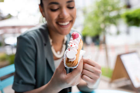 Cheerful african american woman holding eclair with cream outdoors