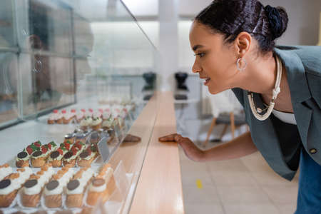 Side view of smiling african american client choosing eclairs near showcase in sweet shopの写真素材