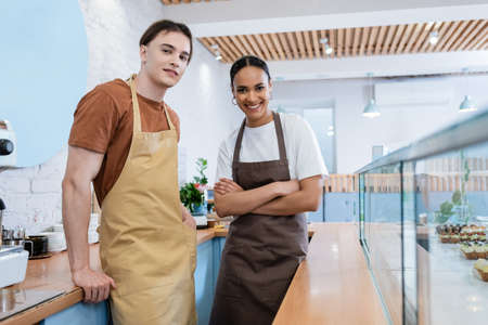 Smiling multiethnic sellers posing near showcase in confectioneryの写真素材