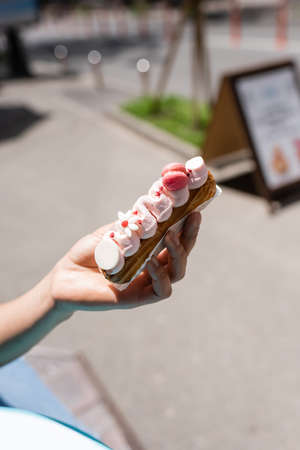Cropped view of african american woman holding eclair with cream on terrace of confectionery