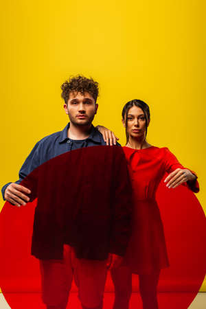 trendy woman and man holding round shape glass while posing isolated on yellow