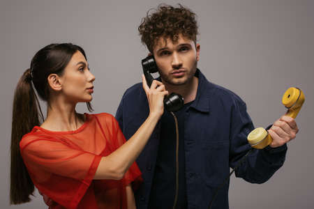 young woman and curly man holding retro handsets while posing isolated on grey