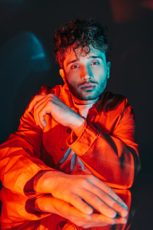 portrait of curly and stylish man in orange shirt posing on blueの写真素材
