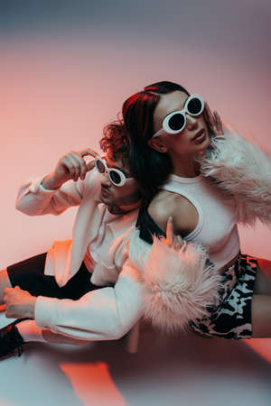 high angle view of stylish man in sunglasses leaning on woman in faux fur jacket on pink and grey