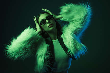 stylish young woman in faux fur jacket and sunglasses posing on blueの写真素材