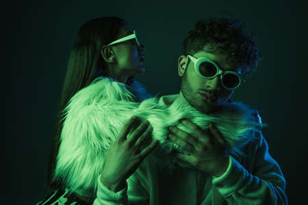 fashionable woman in sunglasses hugging curly man on dark blueの写真素材