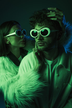 portrait of fashionable models in sunglasses and trendy outfits posing on dark blueの写真素材