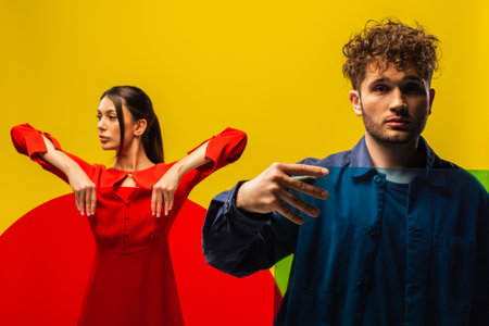 curly man and stylish woman holding glass of different shapes isolated on yellowの写真素材