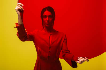 stylish young woman in red dress holding round shape glass isolated on greenの写真素材