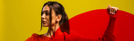 trendy young woman in red dress holding round shape glass isolated on green, bannerの写真素材