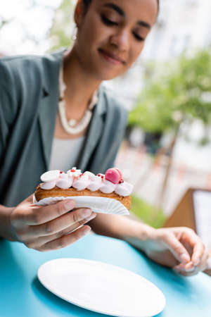 Delicious dessert in hand of blurred african american client on terrace of sweet shopの写真素材