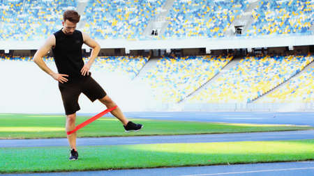 full length of bearded sportsman with hands on hips exercising with resistance band
