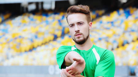 bearded football player in t-shirt stretching hands while warming up on stadium