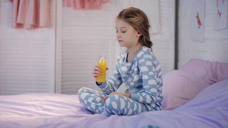 Girl in pajama holding bottle of orange juice on bed in eveningの写真素材