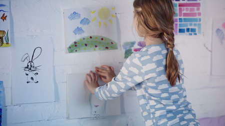 Preteen girl in pajama fastening painting on wall at homeの写真素材