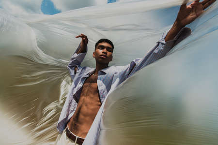 african american man in trendy clothes posing with closed eyes near cellophane film