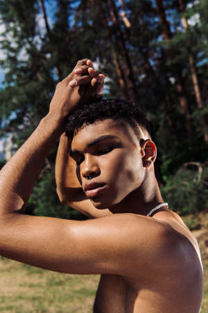 shirtless african american man in piercing posing with closed eyes and hands above headの写真素材