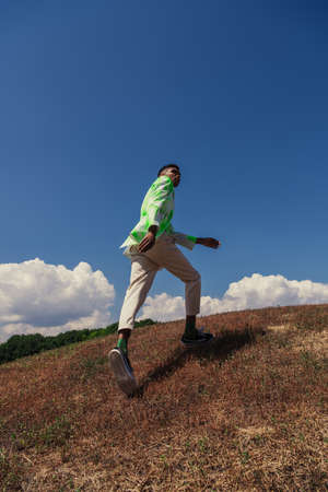 back view of young african american man in summer clothes running in green fieldの写真素材