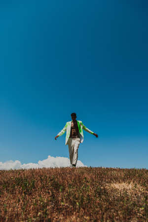 african american man in white trousers and blazer walking under blue sky in field