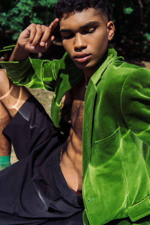 fashionable african american man in green blazer and black shorts sitting outdoorsの写真素材