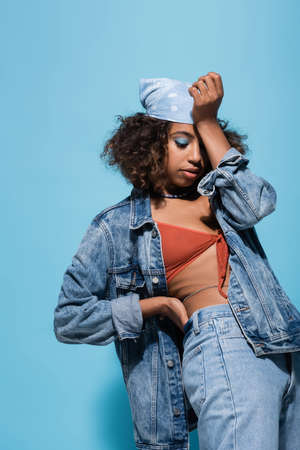 african american woman in swim bra and jacket obscuring face with hand on blue background