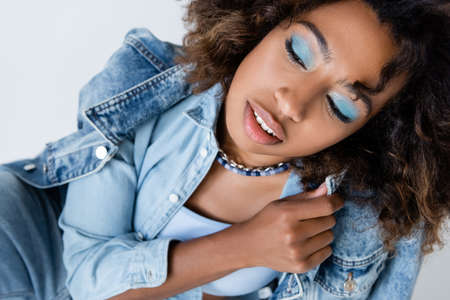 sensual african american woman with blue eye shadows posing with denim garments isolated on greyの写真素材