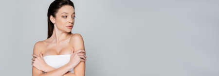 pretty young woman with bare shoulders and makeup looking away isolated on grey, bannerの写真素材