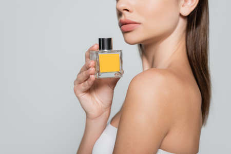 cropped view of woman with bare shoulder holding bottle with perfume isolated on greyの写真素材