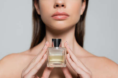 partial view of young woman with naked shoulders holding bottle with luxury perfume isolated on grey