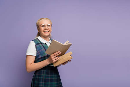 Positive student in eyeglasses and vest holding book isolated on purpleの写真素材