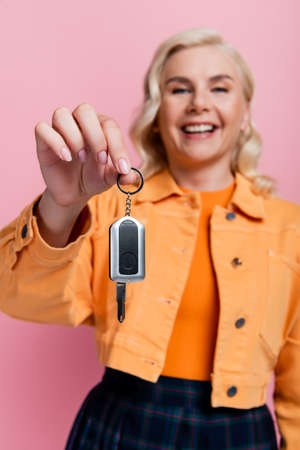 Car key in hand of blurred smiling driver isolated on pink