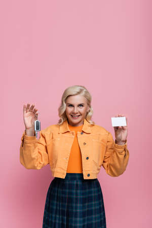 Happy woman holding driving license and car key isolated on pinkの写真素材