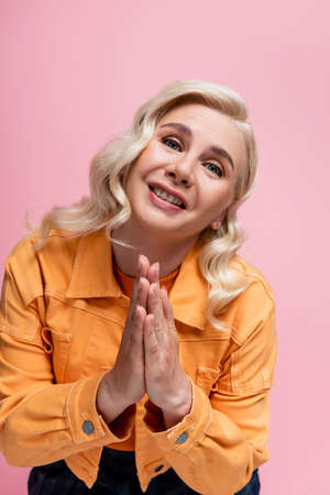 Blonde woman showing praying hands at camera isolated on pink