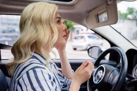 Side view of blonde woman looking at mirror in car