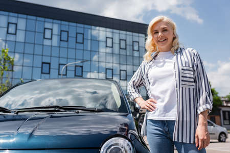 Positive woman holding hand on hip near car on urban street