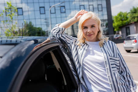 Smiling woman looking at camera near car on urban streetの写真素材