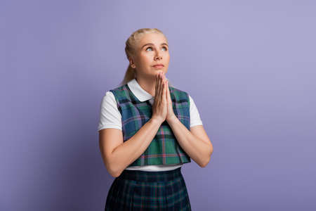 Student in checkered uniform doing praying hands isolated on purpleの写真素材