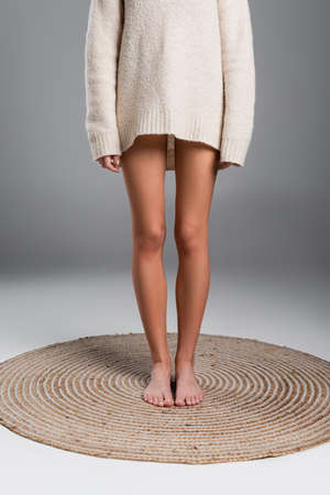 partial view of barefoot woman with naked legs and in long sweater standing on rug on grey backgroundの写真素材