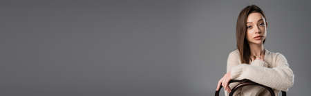 brunette woman in warm and cozy sweater sitting on chair isolated on grey, bannerの写真素材