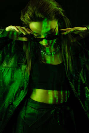 young woman in crop top and leather coat posing with bowed head isolated on blackの写真素材